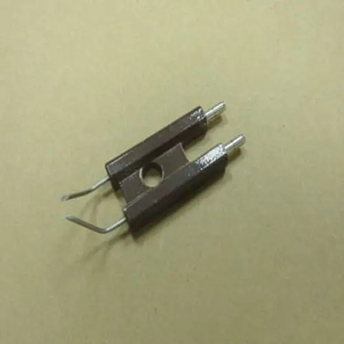 Elektrodenblock mit zwei metallischen Anschlussstiften, auf braunem Untergrund. Produkt von Remeha zur Verwendung in Heizungsanlagen.